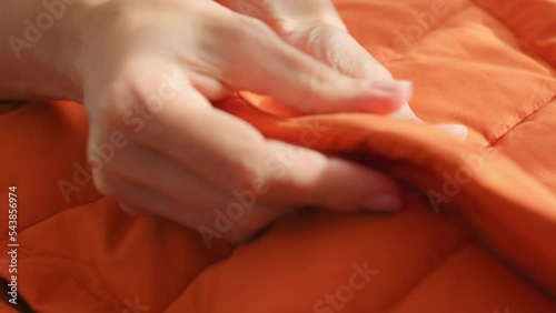 Female hands touching groping material orange waterproof fabric of winter jacket, down jacket. Textile, clothing production, autumn bright jacket. Fashion, Style. Clothes background