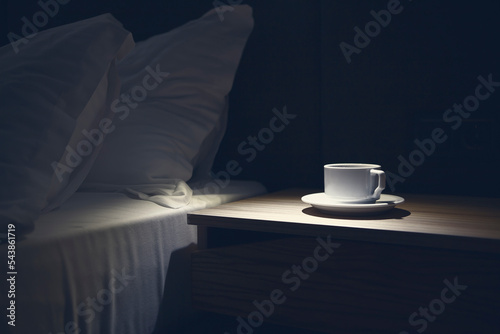 Bedside table with white mug against the bed at night time. Copy and paste, nobody
