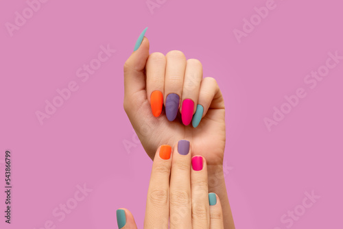 Female hands with colorful nail design. Glitter nail polish manicure: purple, green, pink and orange on pink background