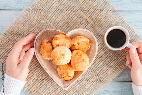 Cheese bread (brazilian Pao de Queijo mineiro) and coffee, heart-shaped plate, woman's hand, top view flat lay photo