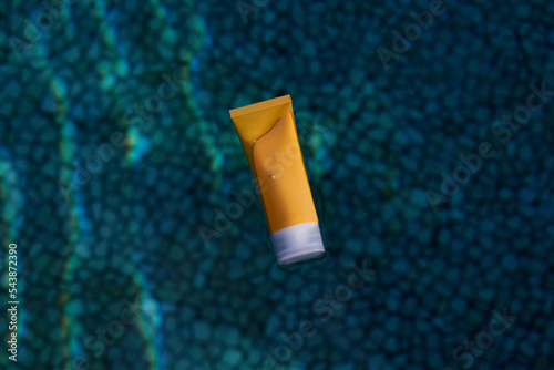 Sun protection cream. Yellow tube of cream with a mockup in the blue transparent water. Skin care and hydration concept. photo