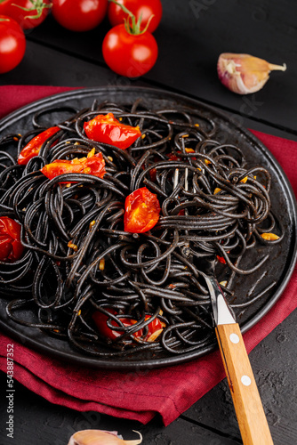 Black spaghetti with vegetables on black plate. Cooked black pasta spaghetti on black boards and ingredients. Close-up