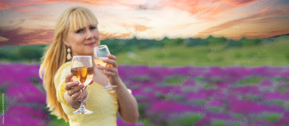 Fototapeta premium A woman drinks wine in a lavender field. Selective focus.