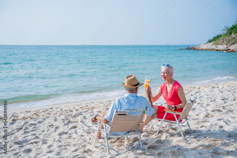 Senior couple relaxing and drink orange juice at tropical beach., Healthy seniors lifestyle concept.