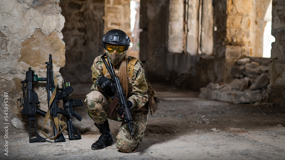 Fototapeta premium A woman in an army uniform sits in an abandoned building and holds a firearm.