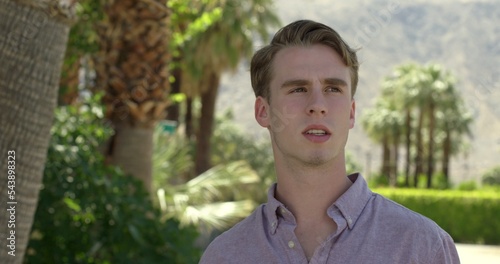 Handsome young man looks around while waiting in Palm Springs, California.  Background of palm trees and mountains