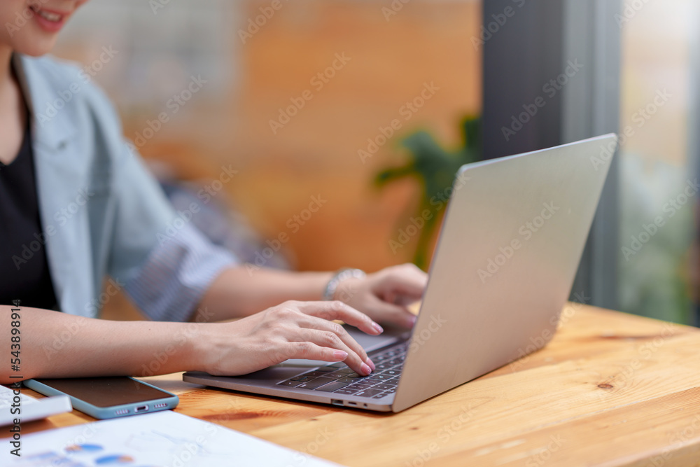Close-up of the hands of a business woman attentively typing on a laptop computer and having a document on the desk in the office. Close-up of the hands of a business woman attentively typing on a laptop computer and having a document on the desk in the office.