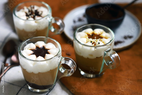 Small mugs with a three-layer coffee-caramel dessert. Delicious pudding in glass cups.