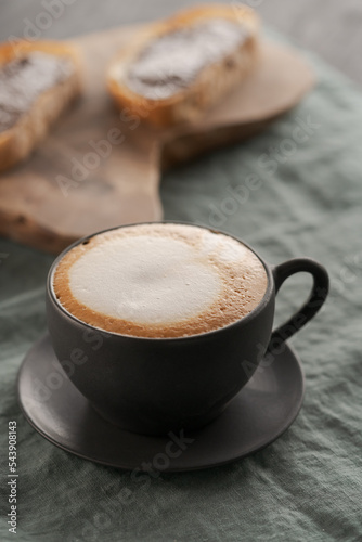 Cappuccino in black cup with ciabatta slices with chocolate spread on background