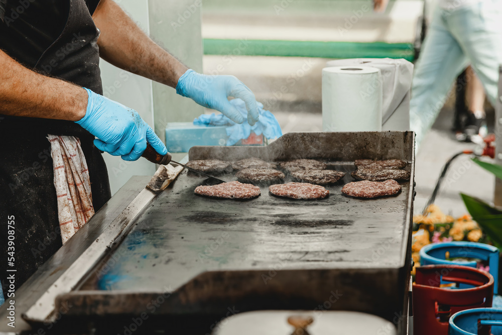 A man fries burger meatballs. Man grills some kind of marinated meat on gas grill during summer time. Meat on the grill is cooked by man's hand in a blue glove. A man fries burger meatballs. Man grills some kind of marinated meat on gas grill during summer time. Meat on the grill is cooked by man's hand in a blue glove.