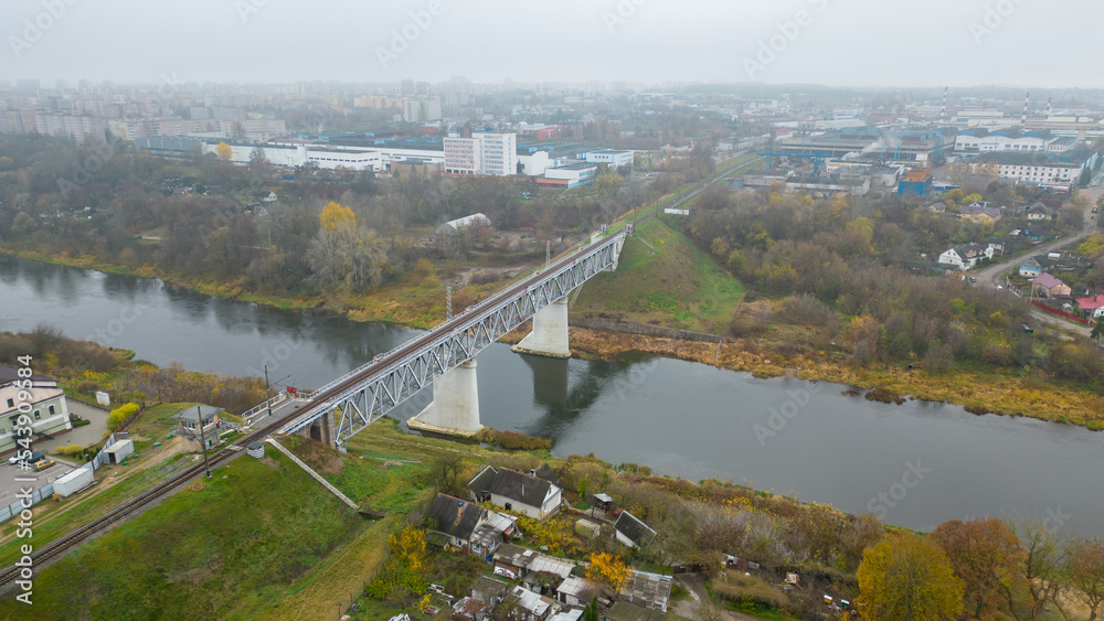 A single-track railway bridge over the river in the city. Top view of the bridge in a beautiful green park. Flying a drone over a railway bridge in the fog. Autumn landscape
