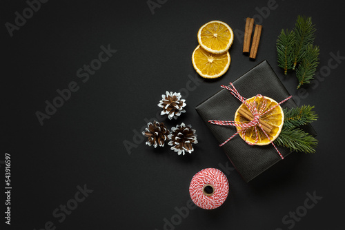 Banner with black gift box with orange and spruce branches, cones and cinnamon on dark background photo