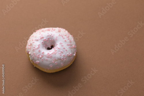 Ciambella con glassa e zuccherini rosa su superficie marrone photo