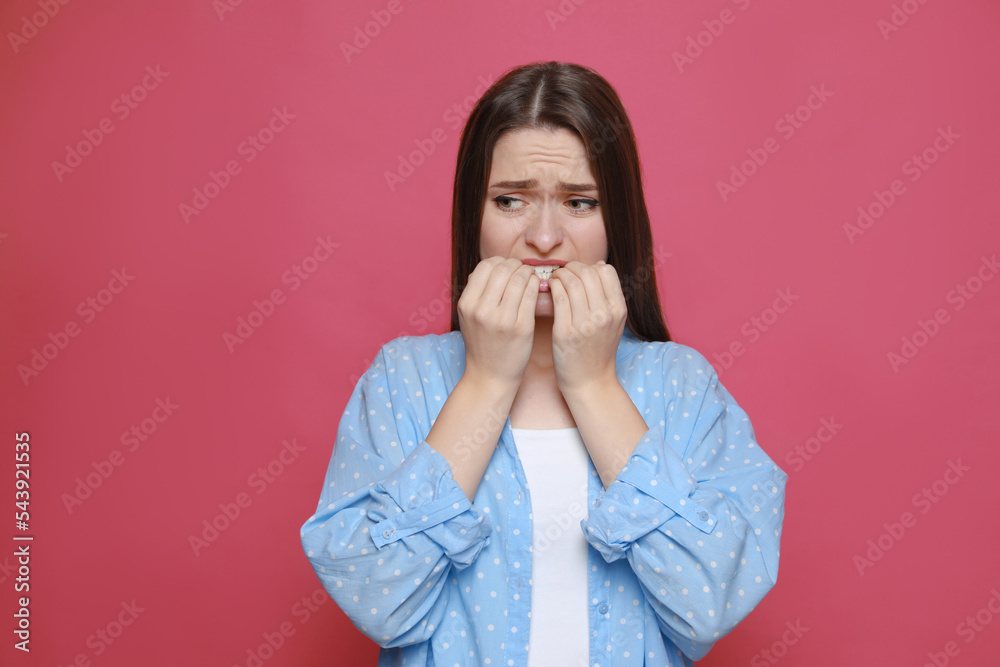 Young woman biting her nails on pink background