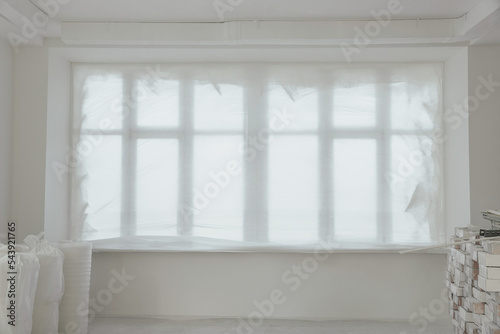 Windows covered by plastic film and building materials in renovated room