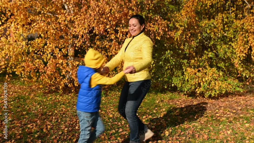 Happy mother and daughter walking in autumn park with orange fallen leaves, having fun, holding hands and whirling, spinning, having fun on a beautiful sunny warm day. Happy childhood and motherhood