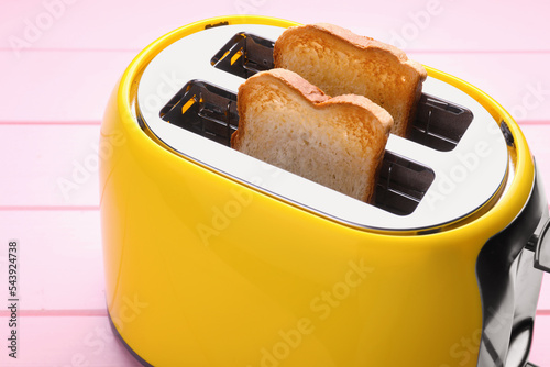 Yellow toaster with roasted bread on pink wooden table, closeup