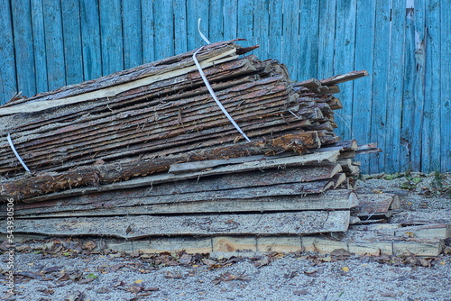 a pile of firewood from long wooden planks and logs on the street near the fence