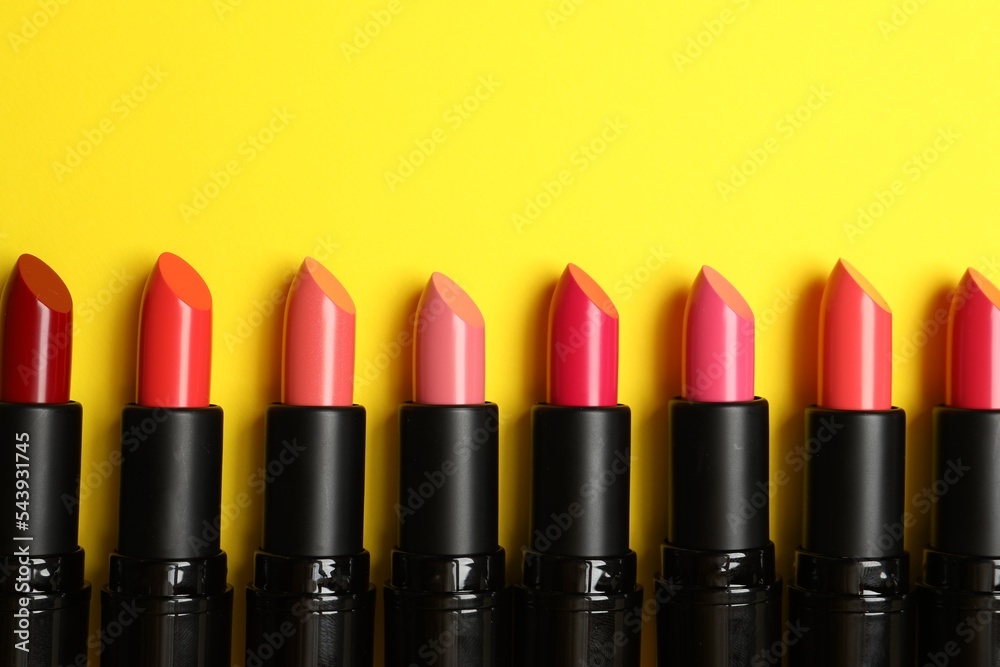 Fototapeta premium Many bright lipsticks on yellow background, flat lay. Space for text