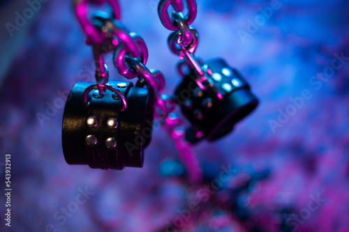 BDSM toys leather handcuffs on a metal chain and neon light