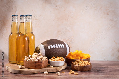 Beer in bottle and snack on wooden table with rugby ball, game night food
