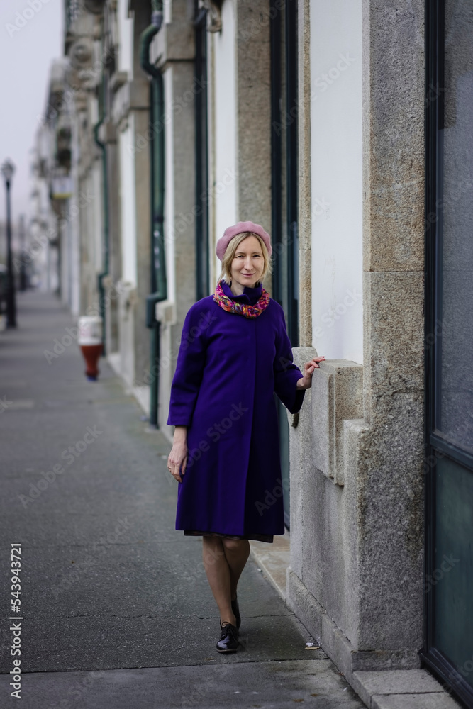 A woman in a lilac coat and beret on a city street.