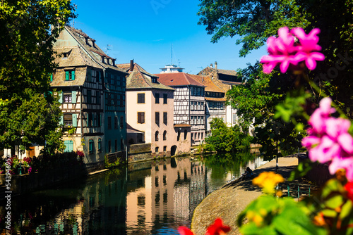 Charming view of residential half-timbered buildings along canals of Strasbourg. Summer streets decorated with bloomy flowers.