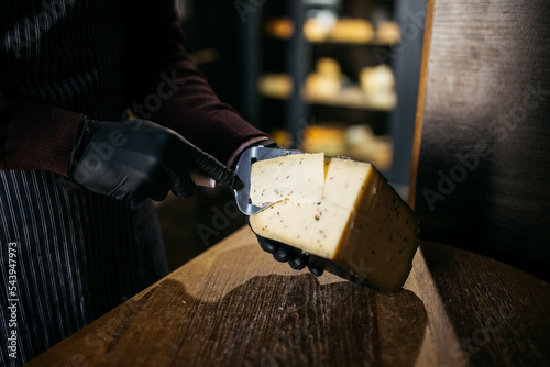 Man slicing a small piece of cheese for taste. A young worker uses a special knife for cheese.