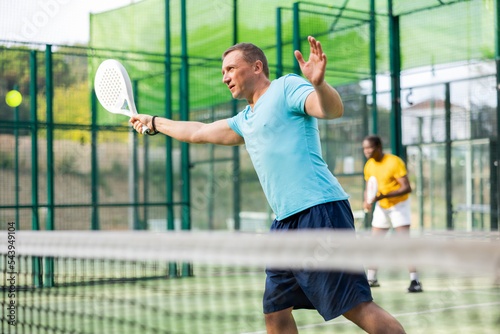 Man in t-shirt playing padel tennis on court. Racket sport training outdoors.