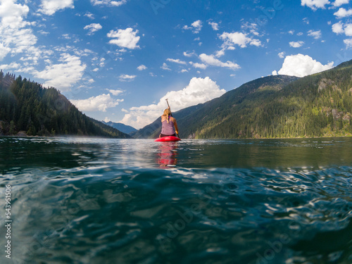 Adventurous athletic woman sitting on a paddle board on a large alpine lake in the Pacific Northwest on a beautiful summer day. 