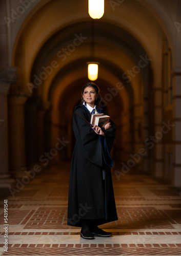 School girl in university hall wearing black robe and holding books with magic wand photo