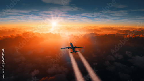 Cinematic view of a commercial airplane making a flight above clouds making a contrail at sunset. Far shot of a cargo aircraft traveling above orange clouds making a smoke out of engines.