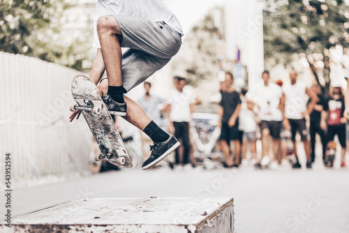 Young skateboarder skateboarding on an object in street. Skateboarding legs doing trick ollie at skate park. Group of friends cheering in the background.