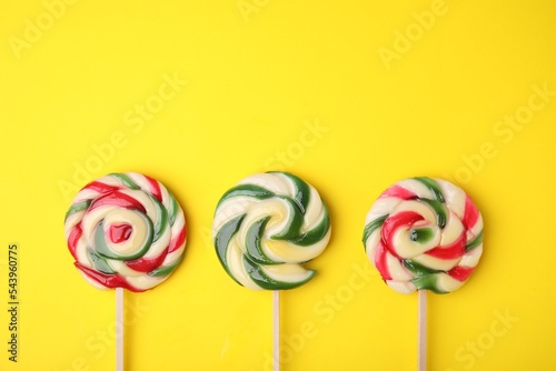 Colorful lollipops on yellow background, flat lay. Space for text