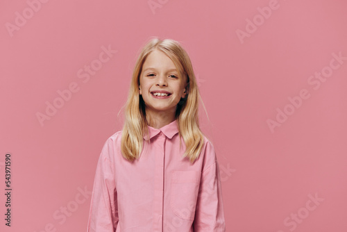 horizontal portrait of a school-age blonde girl in a pink shirt, standing against a one-time background and smiling broadly looking at the camera. Studio photo with empty space for advertising mockup