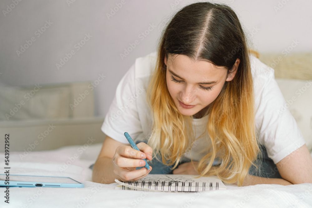 A teenage girl is drawing or doing homework in the bedroom. A teenager studies at home. Back to school A teenage girl is drawing or doing homework in the bedroom. A teenager studies at home. Back to school