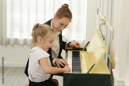 A young white teacher is teaching and training a little girl to play the piano. which is a classic education for kids, learning art.