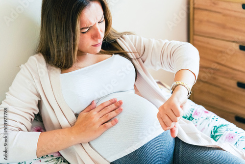 Pregnant pain contractions. Pregnant woman watching clock, holding baby belly. Childbirth time, contractions pain. Pregnancy, medicine health care concept. photo