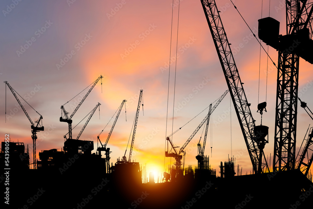 Silhouettes of building construction site and construction cranes with sunset background