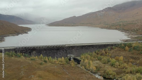 An aerial view of Cluanie Dam on Loch Cluanie in the Northwest Highlands of Scotland at the SE end of Glen Shiel on an overcast day. Flying left to right around the dam face while zooming in photo