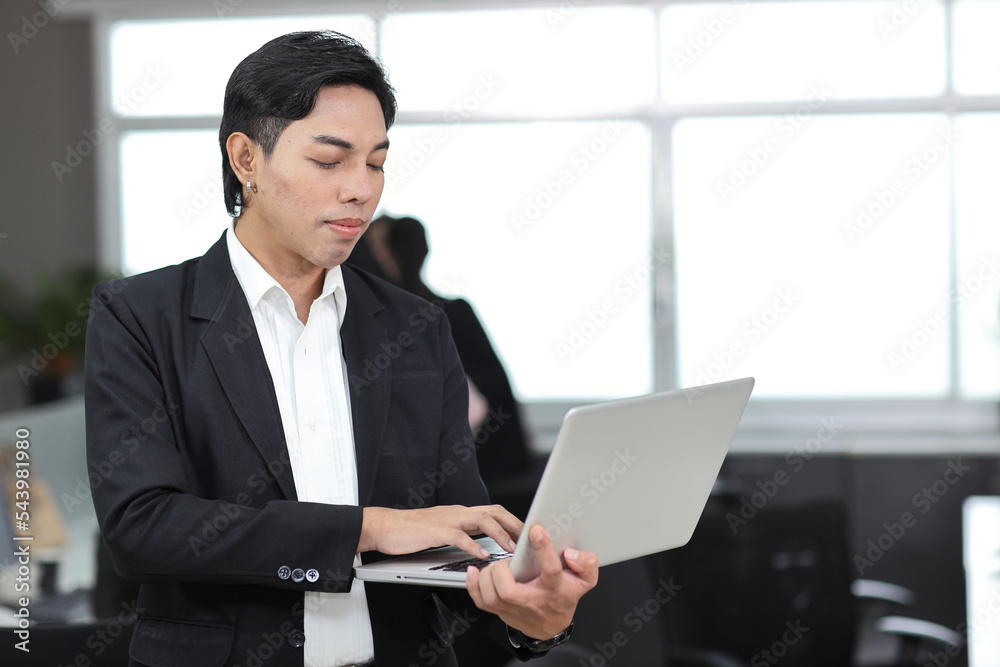 Attractive asian man employee worker in formal dress standing, using computer and looking at camera with coworker at workplace. Businessman smiling and working with notebook in the office. Attractive asian man employee worker in formal dress standing, using computer and looking at camera with coworker at workplace. Businessman smiling and working with notebook in the office.