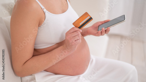 A pregnant woman is holding a smartphone and a credit card. Online shopping concept.