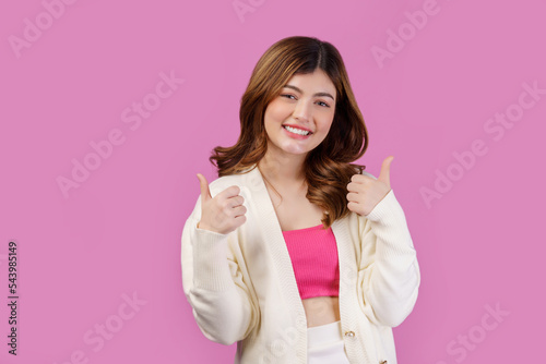 Portrait of Young happy cheerful woman showing thumb up and looking at camera isolated over pink background