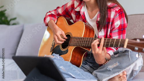 Concept of relaxation with music, Young woman plays acoustic guitar while learning music on tablet