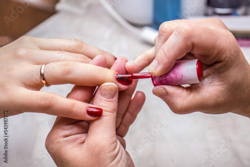 The process of doing a manicure in a spa salon. Applying red nail polish in a nail salon. Manicure  hand care  nail care  red polish. Hand care concept  nail beauty.