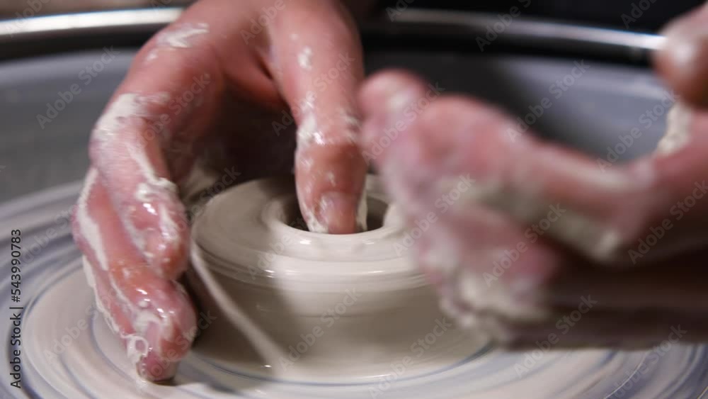 The potter's female hands finger making a hole in the clay. Close-up of working with clay on a potter's wheel. The master creates a mug. The concept of handmade, art and craft The potter's female hands finger making a hole in the clay. Close-up of working with clay on a potter's wheel. The master creates a mug. The concept of handmade, art and craft