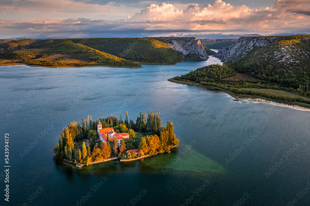 Visovac, Croatia - Aerial view of Visovac Christian monastery island in Krka National Park on a sunny autumn morning with dramatic golden sunrise, autumn foliage and clear turquoise blue water - obrazy, fototapety, plakaty 