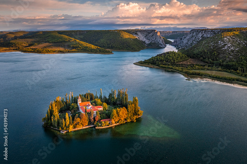 Visovac, Croatia - Aerial view of Visovac Christian monastery island in Krka National Park on a sunny autumn morning with dramatic golden sunrise, autumn foliage and clear turquoise blue water