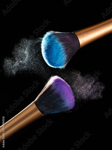 Makeup concept. Stop action view of two makeup brushes applying matching red and gold powder over black background
