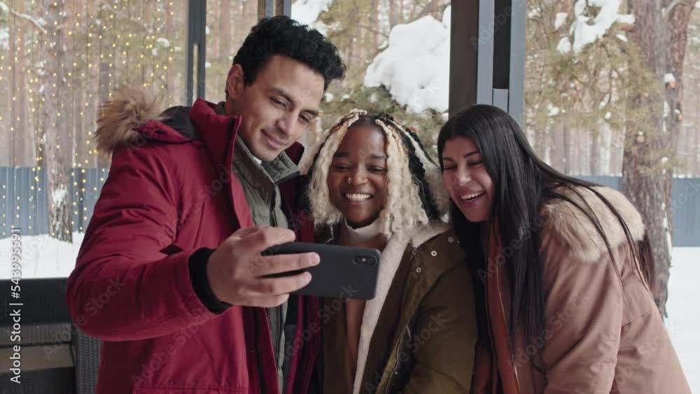 Group of three multi-ethnic friends standing on porch shooting video for blog or having video call on smartphone Group of three multi-ethnic friends standing on porch shooting video for blog or having video call on smartphone